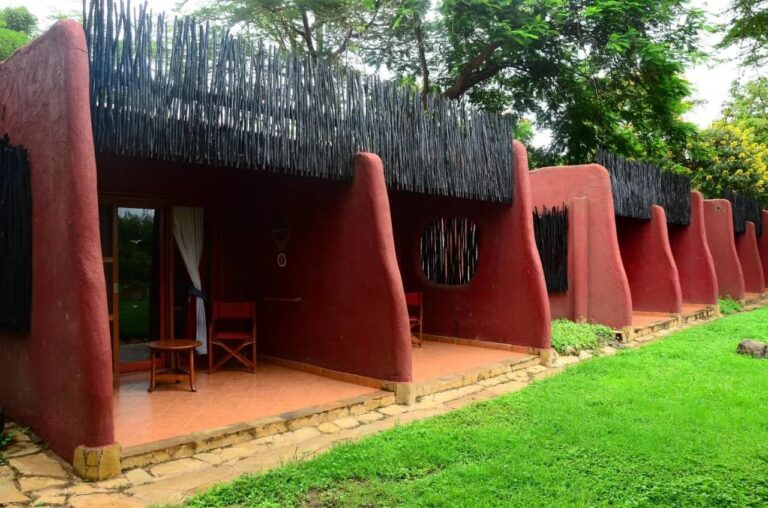Tarasy pokoi Amboseli Serena Safari Lodge między zaokrąglonymi czerwonymi ścianami, naprzeciw trawnika