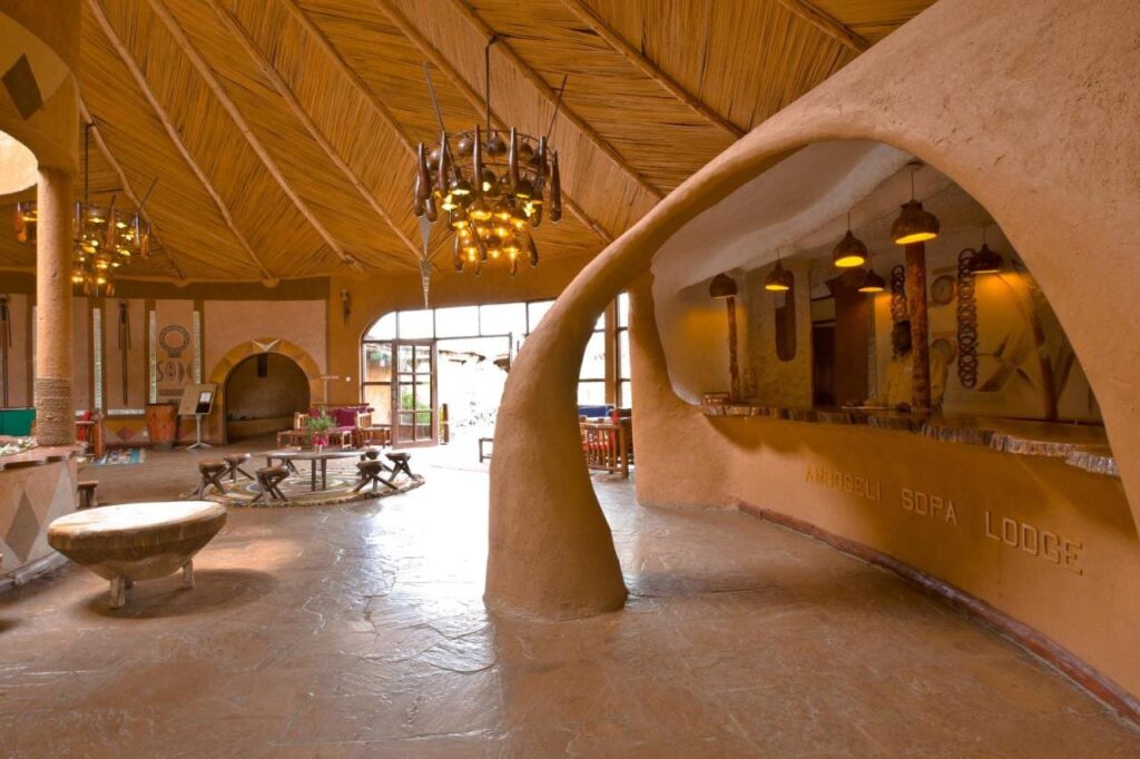 Rzeźbiona gliniana lada recepcji z wygrawerowaną nazwą Amboseli Sopa Lodge, pod sufitem z trzciny