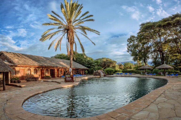 Basen Amboseli Sopa Lodge z palmą, parasolami krytymi strzechą i kamiennym budynkiem