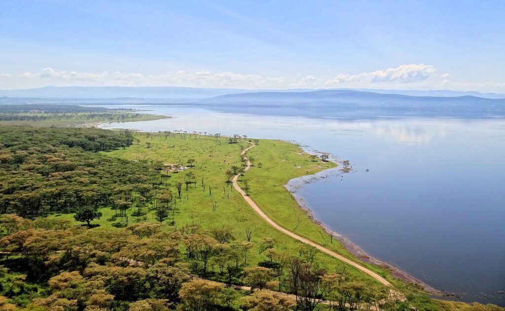 Widok z góry z Baboon Cliff na brzeg jeziora, drogę wzdłuż zielonej łąki usianej zwierzętami, akacjowe zagajniki i jezioro aż po wzgórza