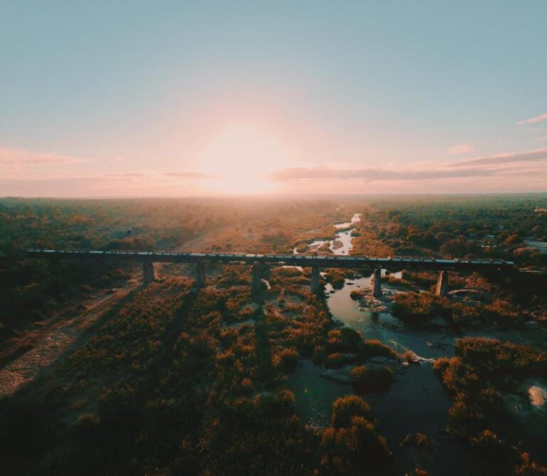 Pociąg Kruger Shalati na moście nad rzeką Selati z lotu ptaka, nad wodą i buszem, przy nisko wiszącym słońcu