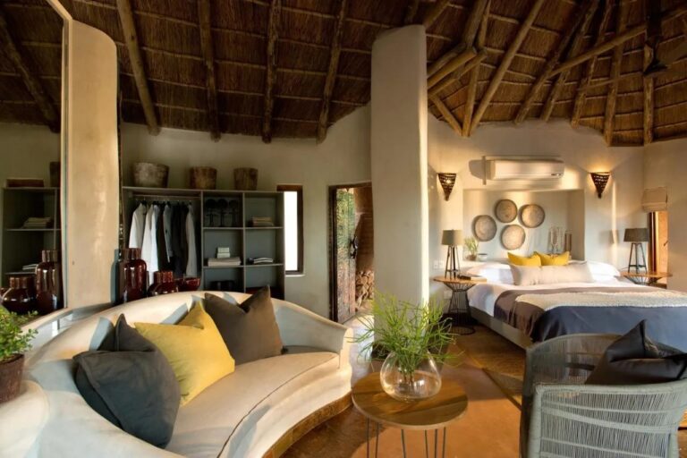 Apartament Madikwe Safari Lodge z białą zaokrągloną kanapą, dużym łóżkiem i otwartą szafą