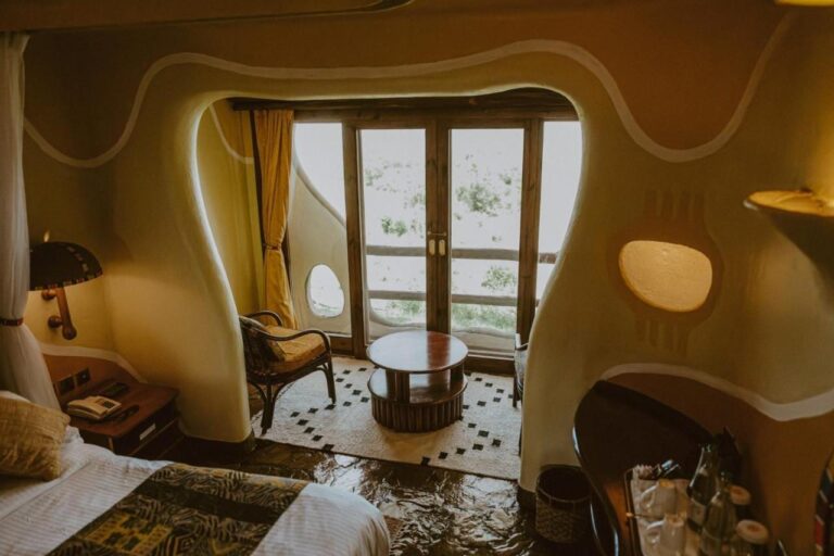 Pokój o zaokrąglonych ścianach w Mara Serena Safari Lodge, z kącikiem wypoczynkowym przed drzwiami na balkon