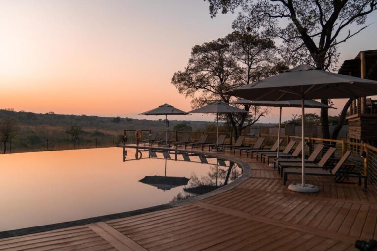 Basen bez krawędzi Mdluli Safari Lodge pod pomarańczowym niebem, otoczony leżakami i parasolami