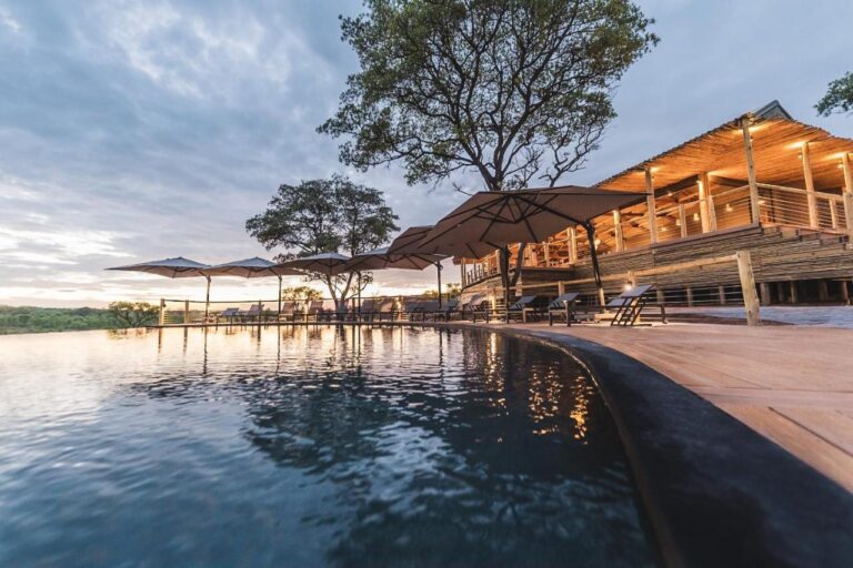 Basen bez krawędzi Mdluli Safari Lodge i oświetlony budynek główny pod zachmurzonym niebem