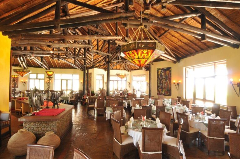 Sala restauracyjna pod konstrukcją z bali, z witrażowymi żyrandolami i stołami nakrytymi białymi obrusami