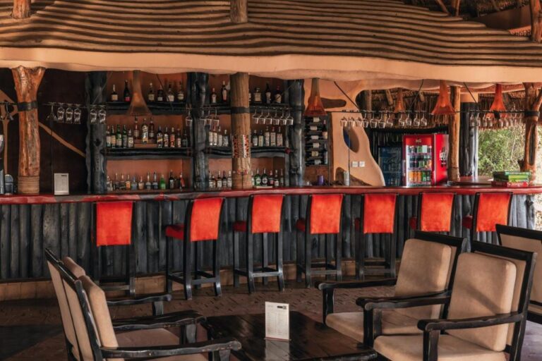 Bar z czerwonymi stołkami i półkami z butelkami, z fotelami na pierwszym planie