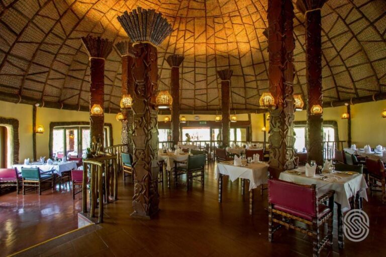 Sala restauracyjna pod kopułą, z drewnianymi kolumnami rzeźbionymi w postacie i stołami nakrytymi białymi obrusami