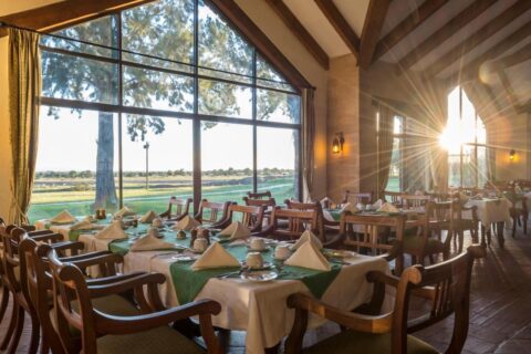 Restauracja Sweetwaters Serena Camp z nakrytymi stołami przed dużym przeszkleniem z widokiem na równinę