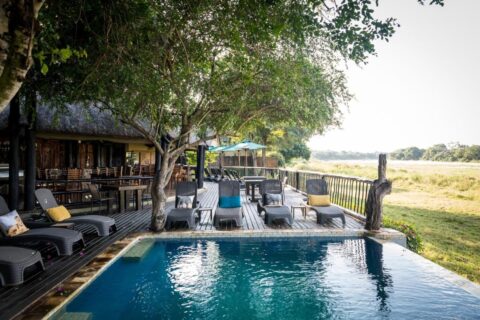Basen Umkumbe Safari Lodge i drewniany taras nad trawiastym brzegiem rzeki