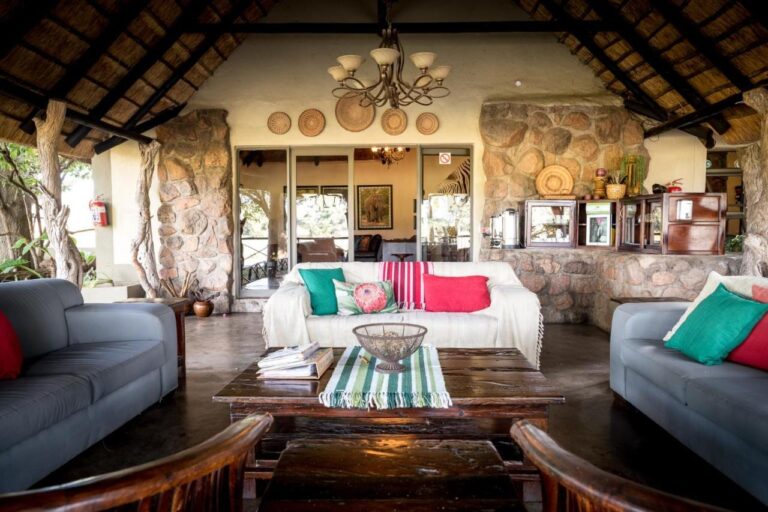 Otwarty salon Umkumbe Safari Lodge pod strzechą, z szarymi kanapami i kamiennymi ścianami